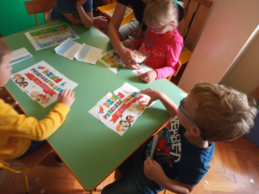 Na fotografii czwórka dzieci siedzących przy stoliku układa kolorowe puzzle