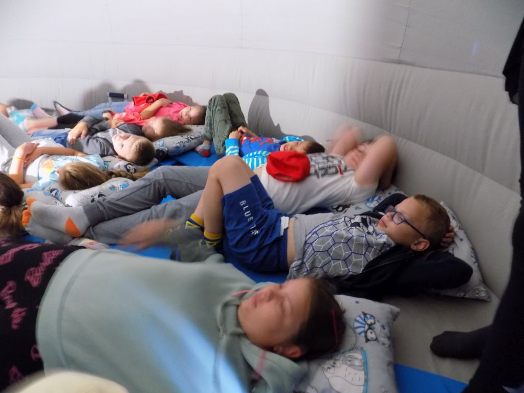 Fotografia przedstawia uczestników zajęć leżących w mobilnym planetarium. Leżą na poduszkach
