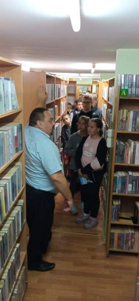 Na zdjęciu widać dyrektora Biblioteki oprowadzającego dzieci po bibliotece