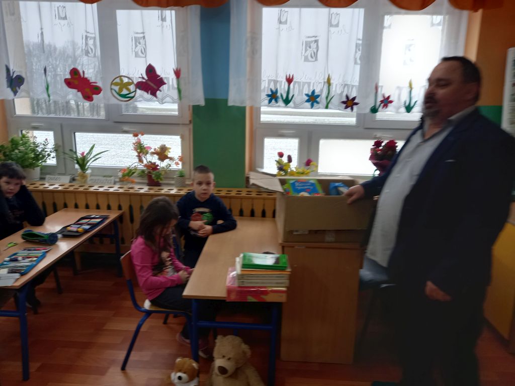 Zdjęcie przedstawia dyrektora biblioteki stojącego w klasie przed dziećmi w trakcie prowadzenia zajęć lekcyjnych