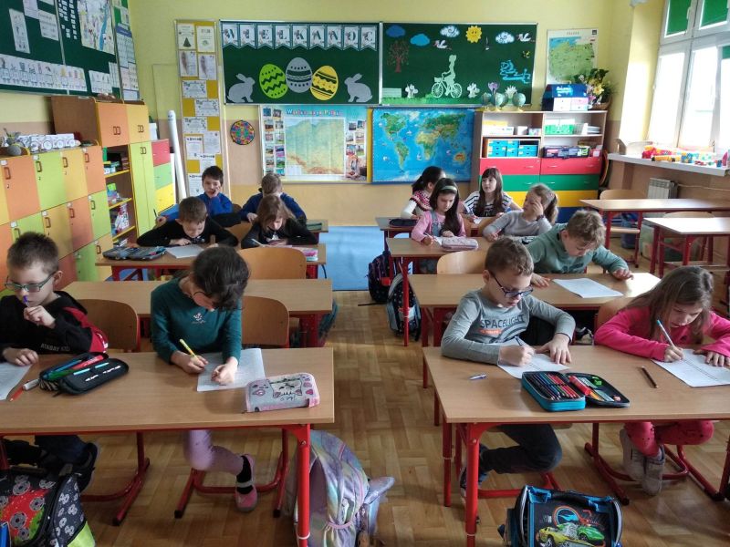 Zdjęcie przedstawia dzieci siedzące w ławkach szkolnych w trakcie lekcji