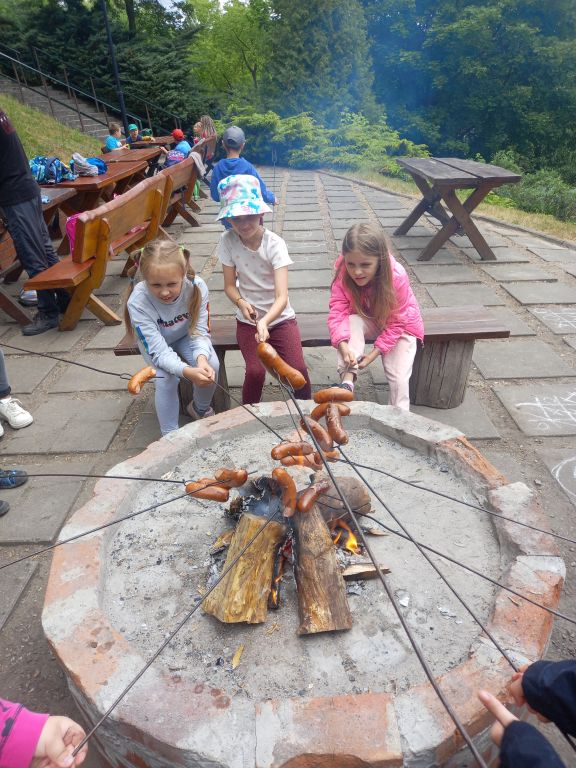 Zdjęcie przedstawia dzieci w trakcie pieczenia kiełbasek nad ognikiem