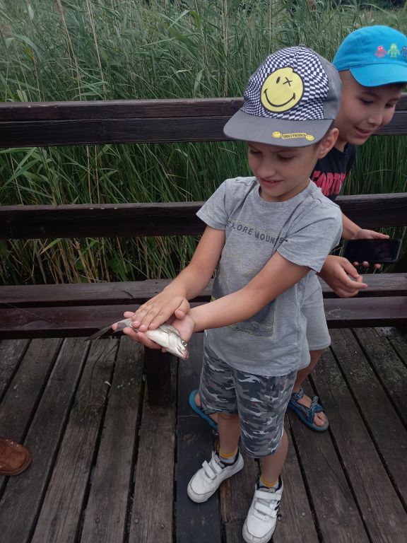 Zdjęcie przedstawia chłopca trzymającego w ręku złowioną rybę