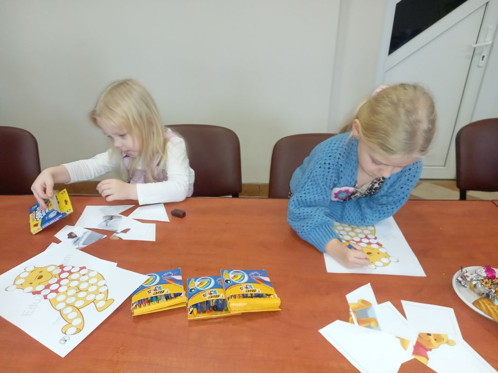 Zdjęcie przedstawia przedszkolaków siedzących przy stołach w trakcie kolorowania obrazków