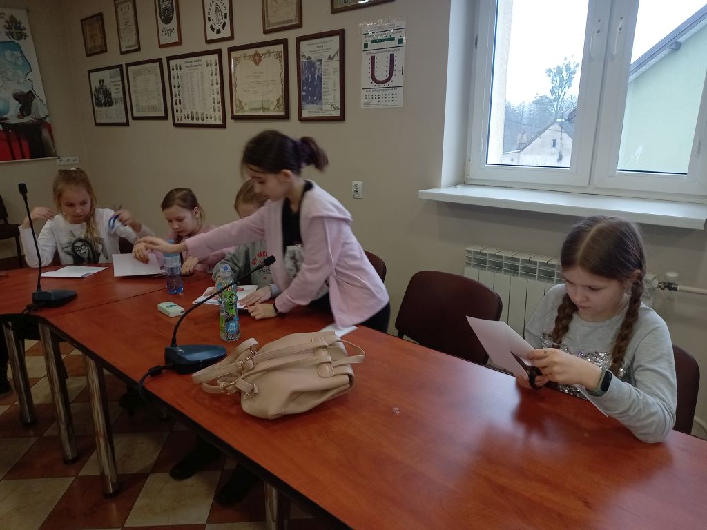 Zdjęcie przedstawia uczestników zajęć origami wykonujących swoje prace na stolikach