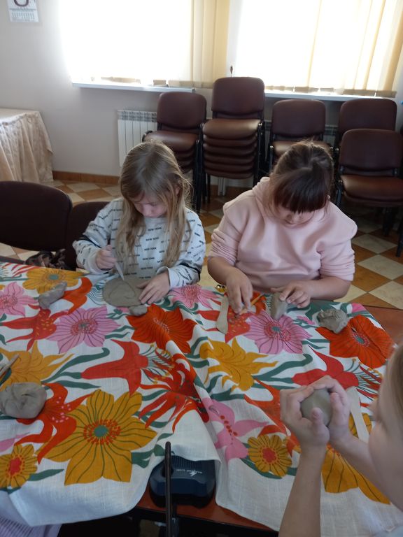Zdjęcie przedstawia dzieci siedzące przy stoliku w trakcie lepienia z gliny