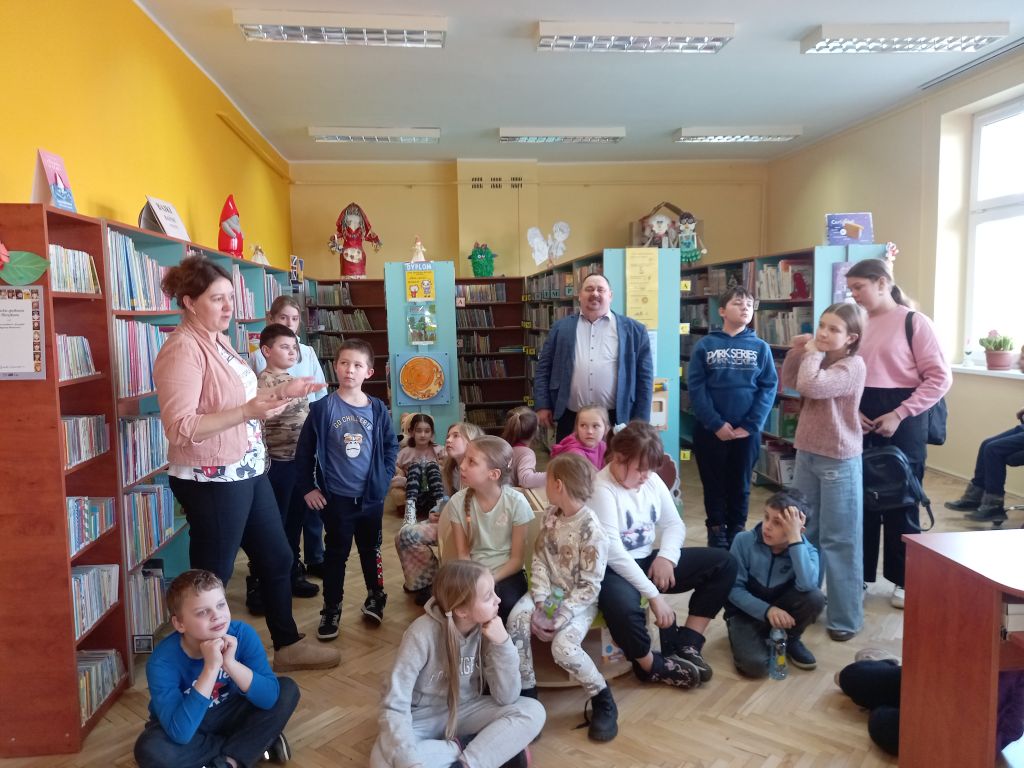 Zdjęcie przedstawia grupkę dzieci i pracowników Biblioteki w Rypinie oraz dyrektora Biblioteki ze Skępego w trakcie zajęć w bibliotece