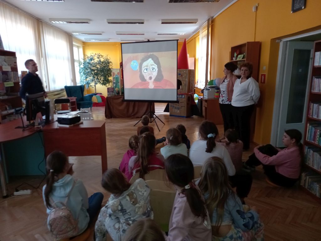Zdjęcie przedstawia grupkę dzieci i pracowników Biblioteki w Rypinie w trakcie prezentacji multimedialnej