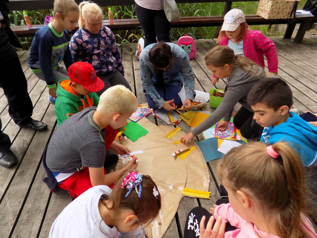 grupka dzieci kolorujące na pomoście pracę z papieru w postaci ryby