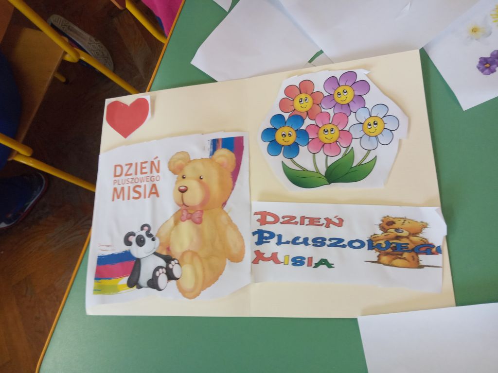 Fotografia przedstawia kolorową, wyklejaną obrazkami kwiatów i misiów laurkę wykonaną przez przedszkolaka w czasie zajęć
