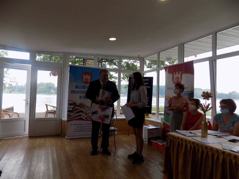 Zdjęcie przedstawia Członka Zarządu Województwa Kujawsko Pomorskiego wręczającego nagrodę uczestniczce konkursu