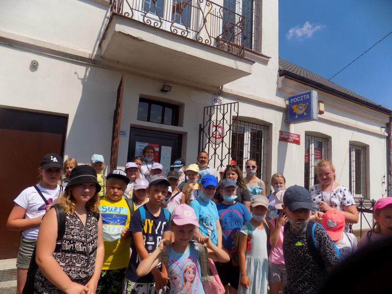 Na zdjęciu widać grupę dzieci  wraz z opiekunami stojących przed budynkiem poczty w Skępem