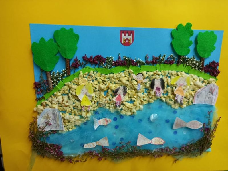 Zdjęcie przedstawia pracę laureat pierwszego miejsca miejsc w kategorii do 6 lat  Zofii i Aleksandry Redeckich. Praca wykonana technika mieszaną przedstawia dzieci bawiące się na plaży nad jeziorem. W jeziorze widać pływające ryby.. W tle widać drzewa i herb Skępego