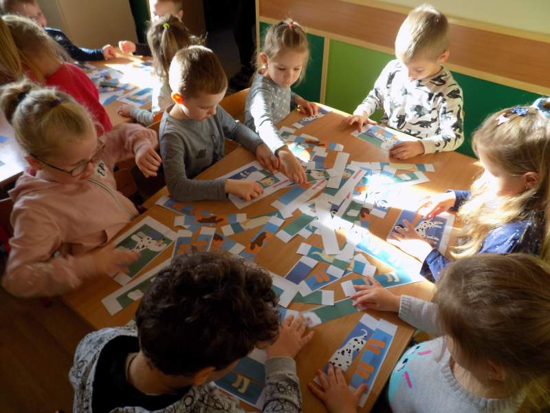 Na zdjęciu widać dzieci siedzące przy stoliku i układające z puzzli obrazek pieska