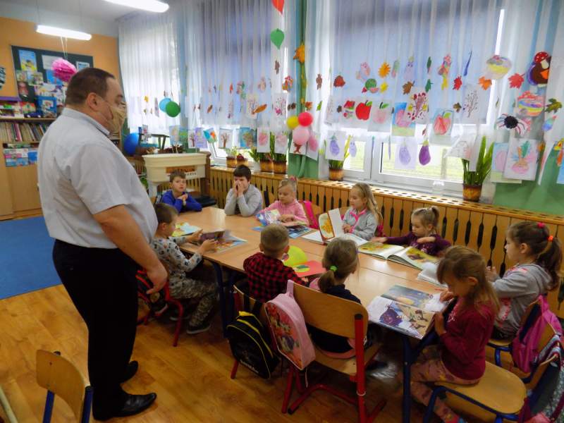 Zdjęcie przedstawia zajęcia w Szkole Podstawowej w Czermnie. Na zdjęciu widać dyrektora biblioteki , który stoi przy dzieciach siedzących w szkolnych ławkach