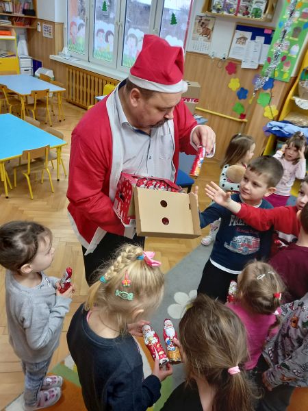 Zdjęcie przedstawia Dyrektora biblioteki przebranego w strój Mikołaja wręczającego dzieciom czekoladowe Mikołaje w Przedszkolu