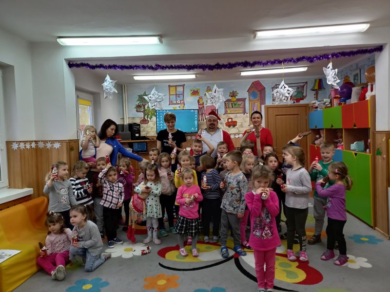 Zdjęcie przedstawia przedszkolaków i opiekunów wraz dyrektorem przebranym w strój Mikołaja pozujących do wspólnej fotografii