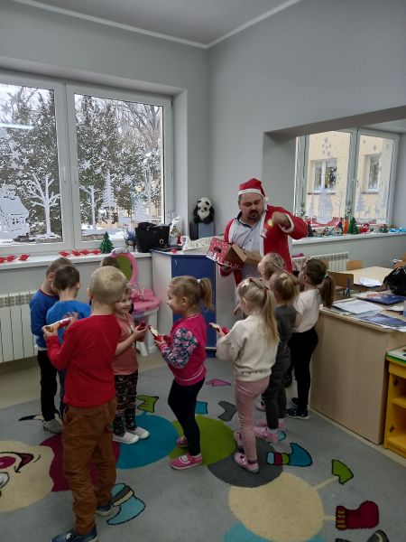 Zdjęcie przedstawia Dyrektora Biblioteki przebranego w strój Mikołaja wręczającego dzieciom w przedszkolu czekoladowe Mikołaje
