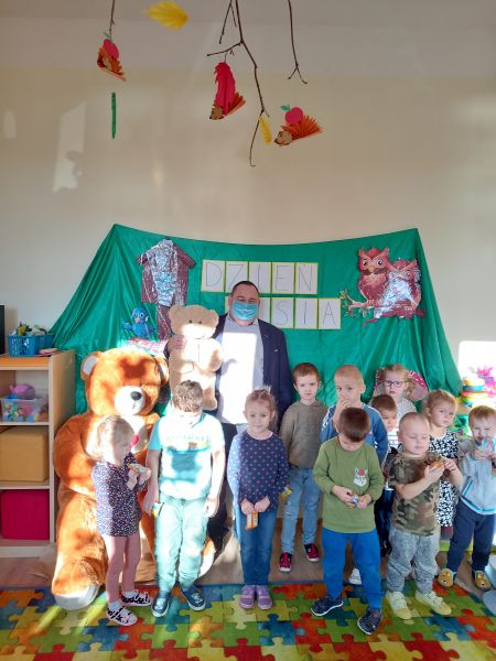 Zdjęcie przedstawia dzieci stojące pod ścianą wraz z dyrektorem biblioteki pozujące na tle dużego, pluszowego misia do zdjęcia