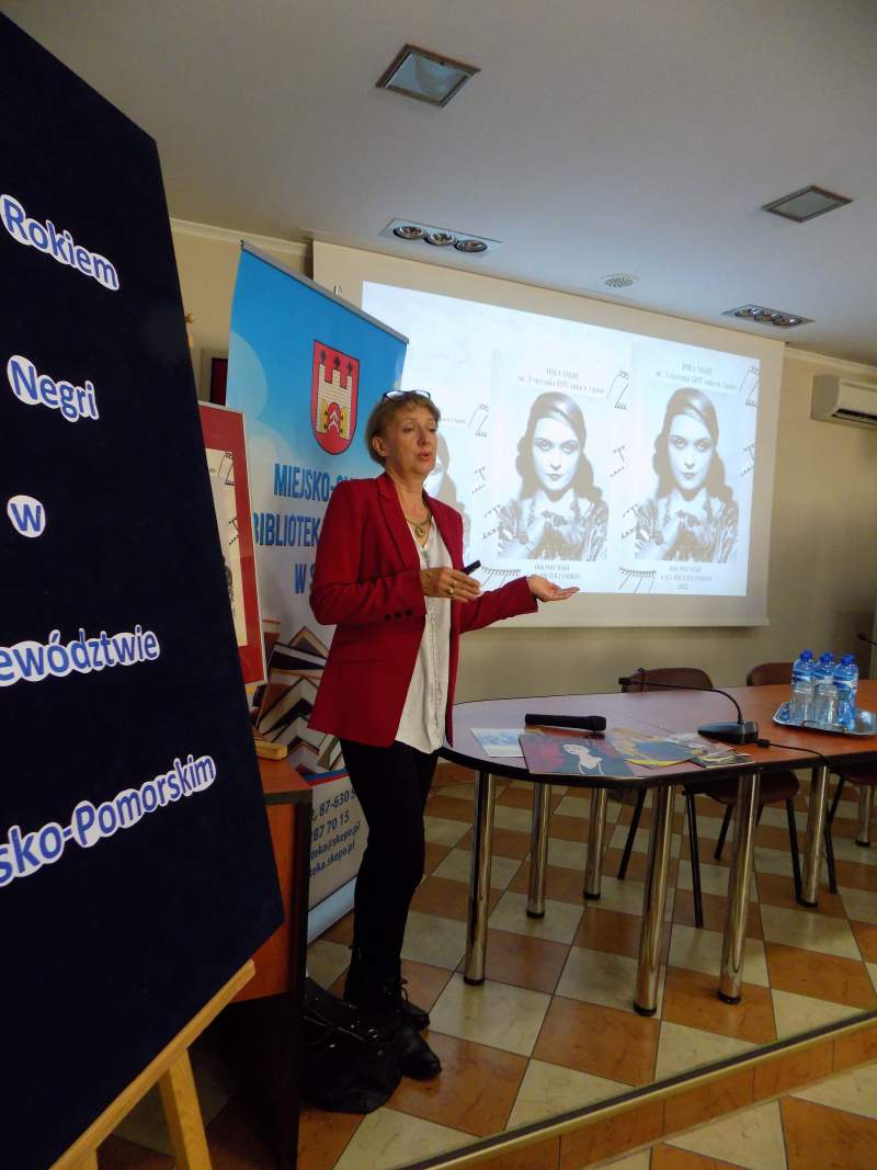 Fotografia przedstawia Dorotę Łańcucką omawiającą slajdy wyświetlone na tablicy w takcie wykładu