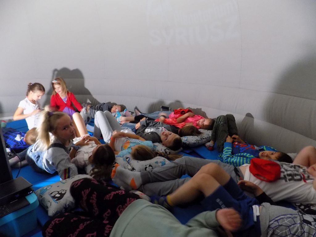 Fotografia przedstawia uczestników zajęć leżących w mobilnym planetarium