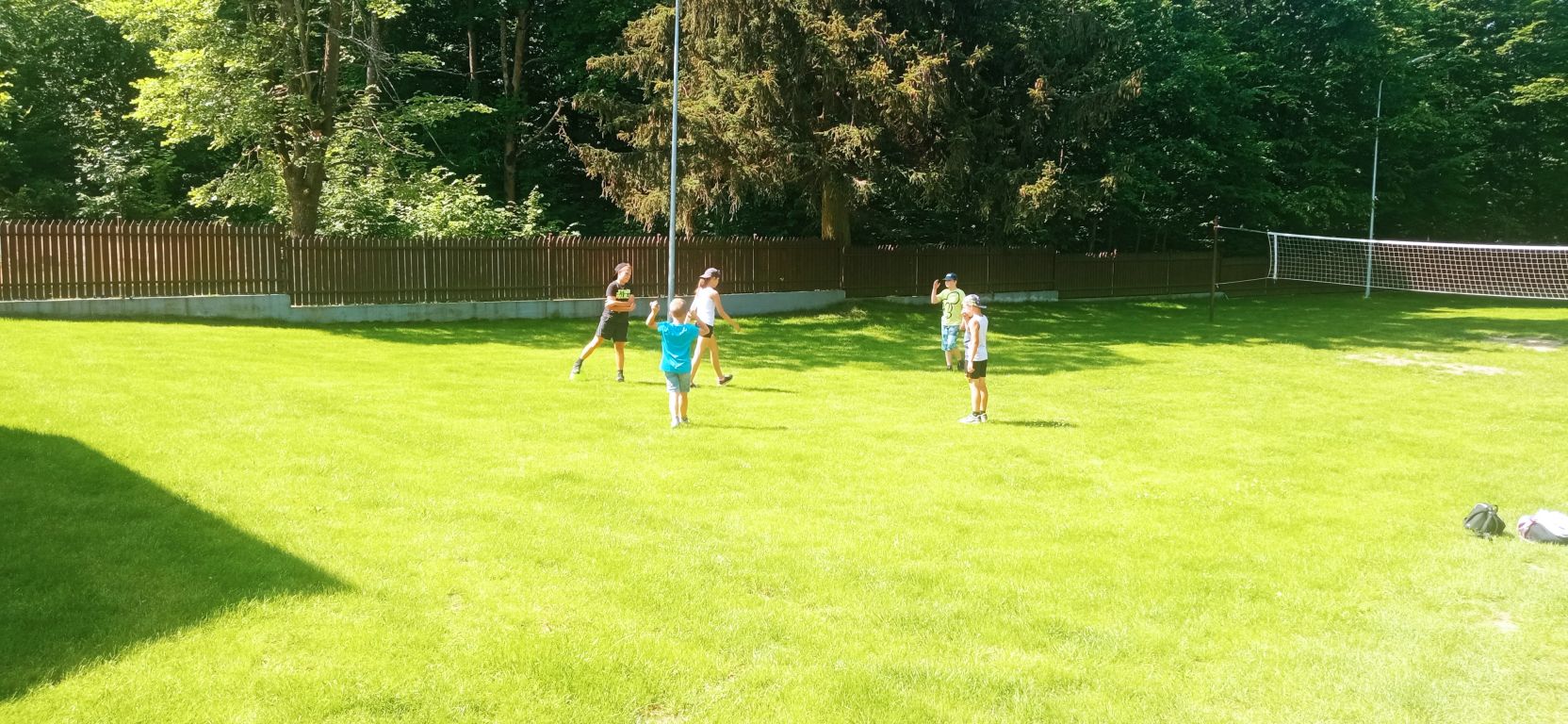 Fotografia przedstawia uczestników zajęć grających na boisku w Ośrodku Wypoczynkowym w Górznie. Biegają po zielonej trawie za piłką