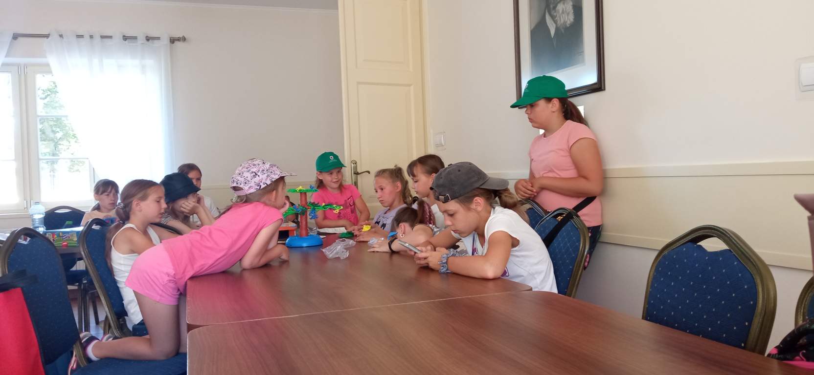 Fotografia przedstawia uczestników zajęć grających w gry planszowe przy stołach wewnątrz biblioteki