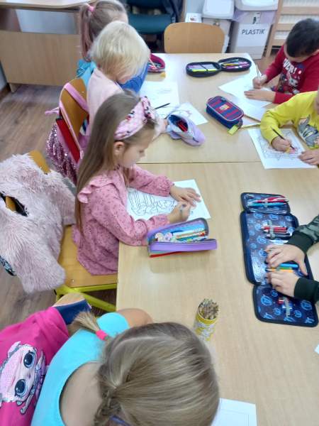 Na zdjęciu widać dziewczynki oraz chłopców, którzy wspólnie kolorują tematyczne rysunki siedząc przy stolikach