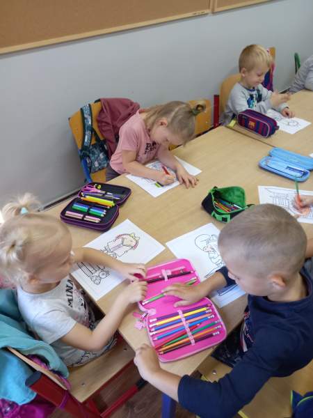 Na zdjęciu widać przedszkolaki dzielące się swoimi kredkami , aby pokolorować rysunki.