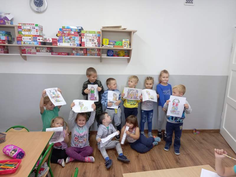 Zdjęcie przedstawia grupkę dzieci które z dumą pokazują swoje rysunki
