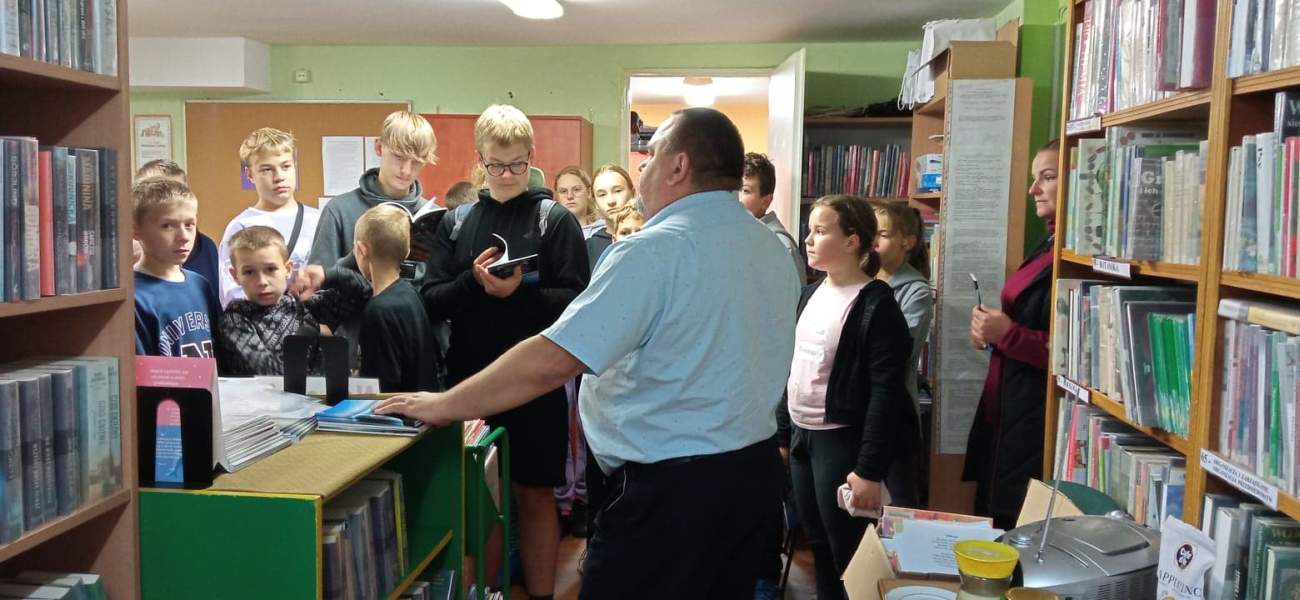 Na zdjęciu widać dzieci oraz ich opiekunów w bibliotece słuchające dyrektora