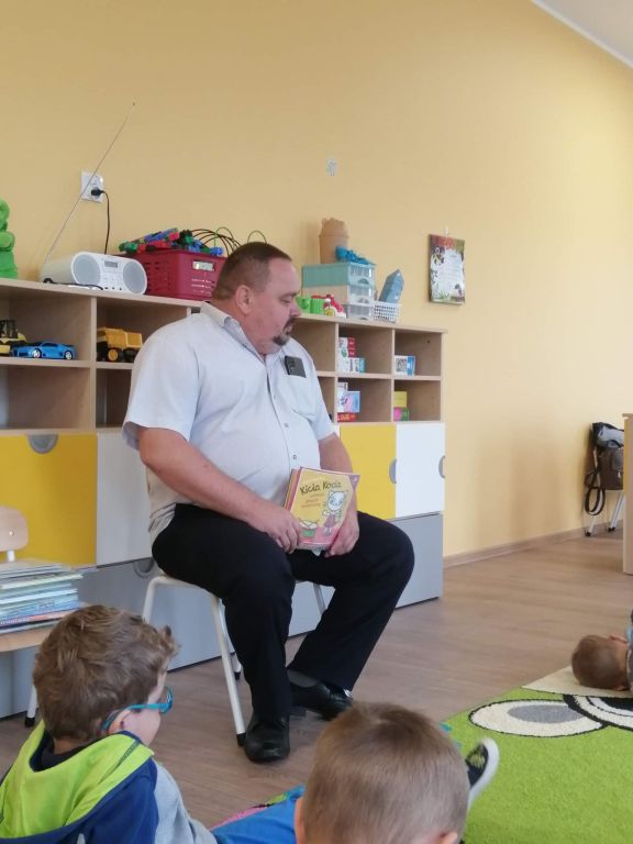 Dyrektor biblioteki siedzi na krześle w przedszkolu i pokazuje dzieciom kolorową książeczkę