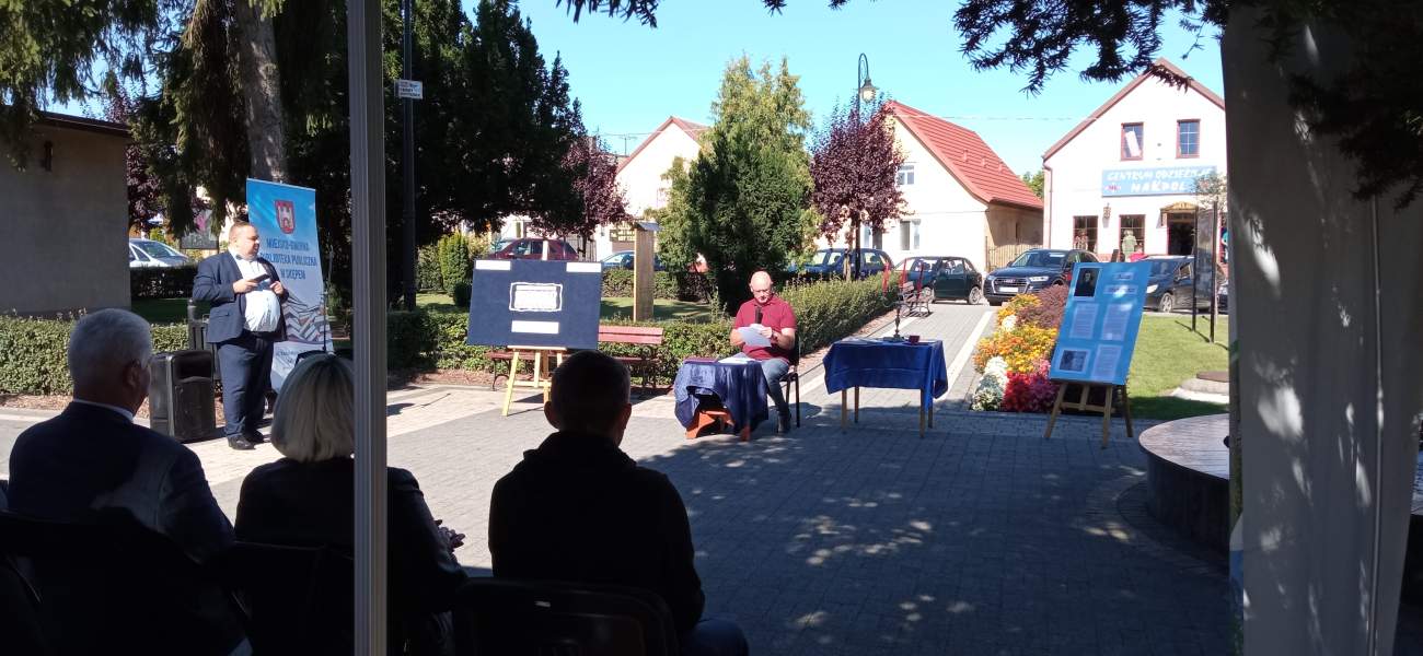 Zdjęcie przedstawia radnego Rady Miejskiej w Skępem Andrzeja Podlasa odczytującego wiersz Adama Mickiewicza. W tle widać scenerię rynku