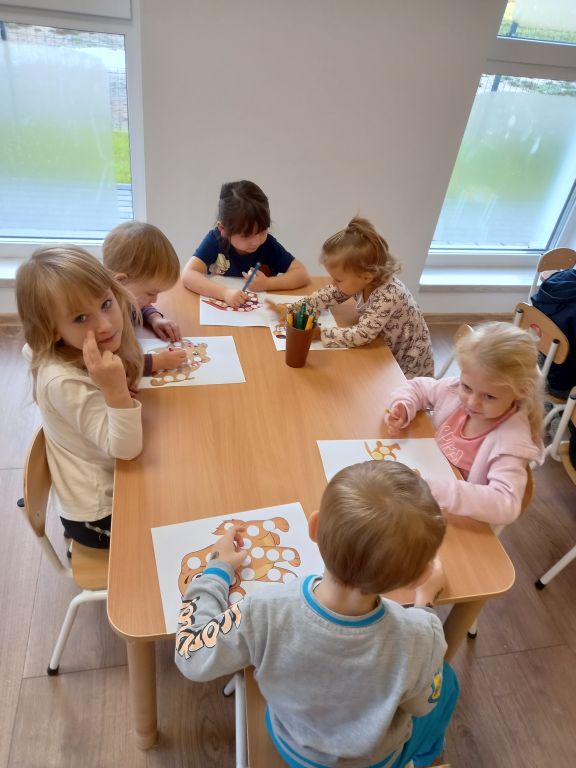 Fotografia przedstawia dzieci siedzące przy stoliku w przedszkolu w trakcie zajęć plastycznych