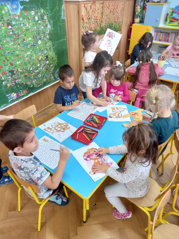 Zdjęcie przedstawia dzieci siedzące w przedszkolu przy stolikach. Dzieci  kolorują szablony z podobizną pieska