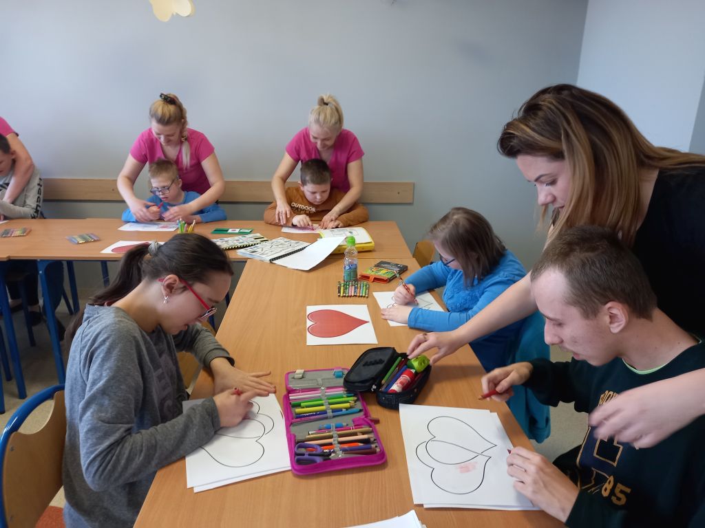 Fotografia przedstawia dzieci siedzące przy stolikach kolorujące obrazki 