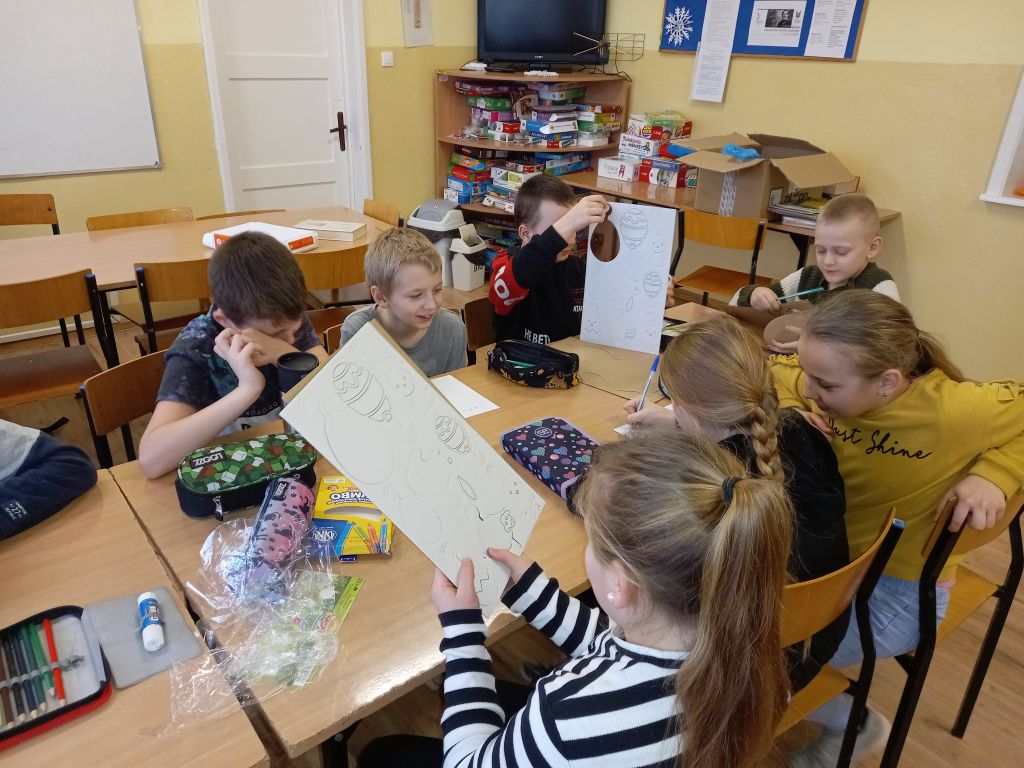 Fotografia przedstawia dzieci siedzące przy stolikach w trakcie zajęć