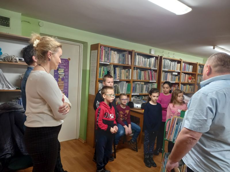 Fotografia przedstawia dzieci wraz z opiekunami i dyrektorem biblioteki w bibliotece