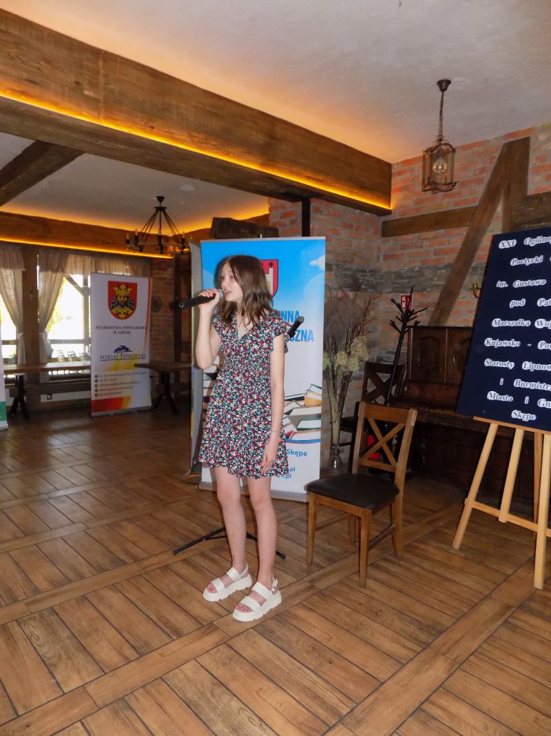 Fotografia przedstawia stojącą dziewczynę i śpiewającą piosenkę w Sali w której odbywa się gala konkursowa