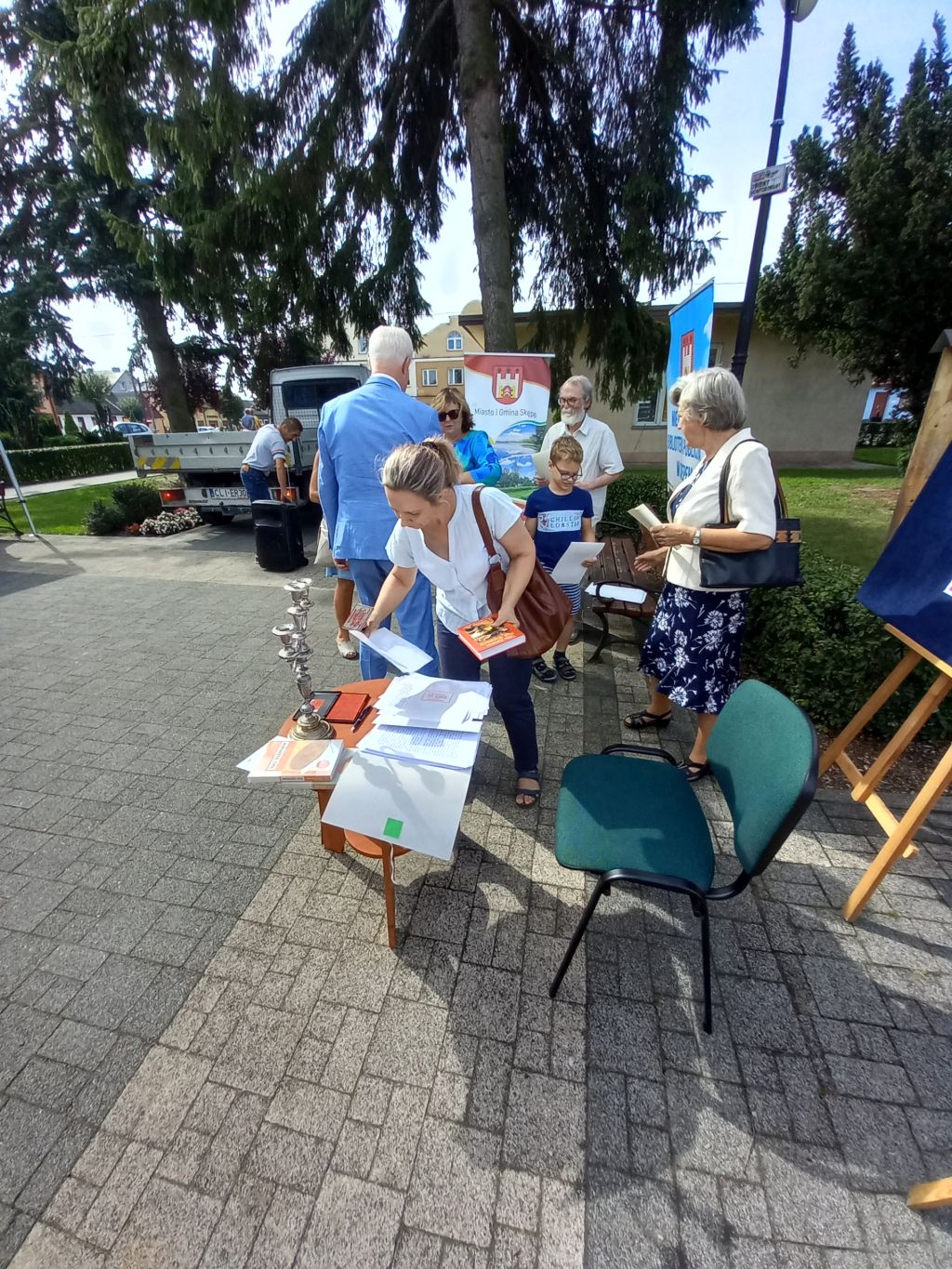 Na zdjęciu widać uczestników Narodowego Czytania pieczętujących na skwerku na stoliku pieczęcią przyniesione książki