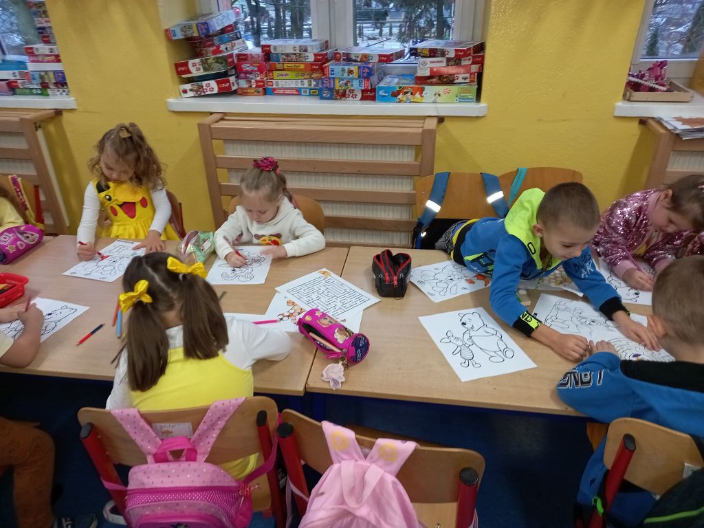 Zdjęcie przedstawia dzieci siedzące w klasie przy stolikach w trakcie zajęć plastycznych