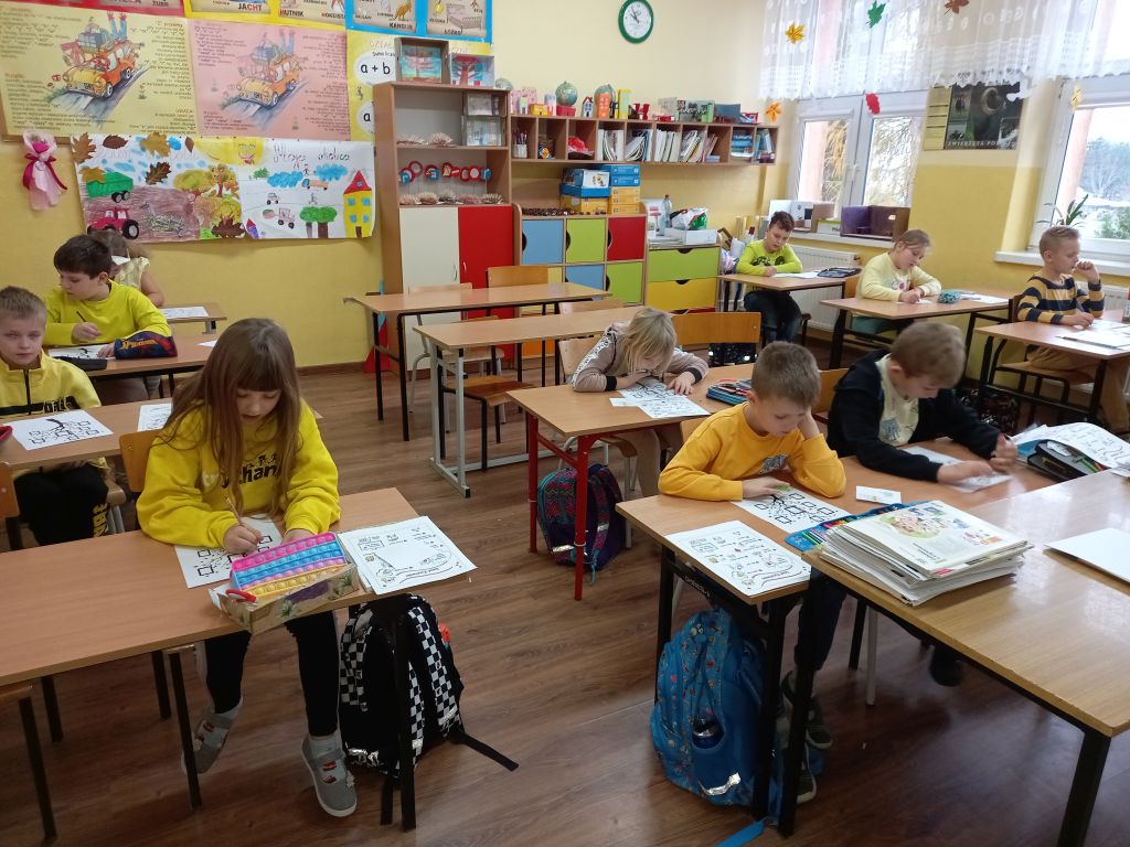 Zdjęcie przedstawia dzieci siedzące na dywanie w klasie w trakcie lekcji