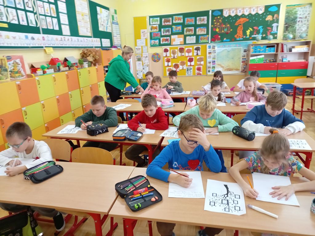 Zdjęcie przedstawia widok ogólny na dzieci siedzące w ławkach w klasie w trakcie lekcji