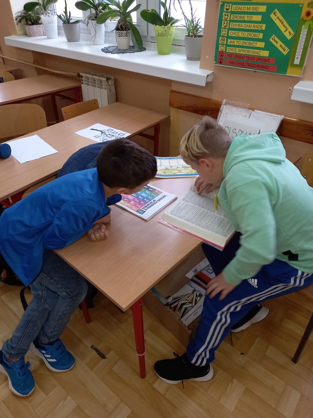Zdjęcie przedstawia dwóch uczniów przy szkolnej ławce w trakcie pracy ze słownikiem