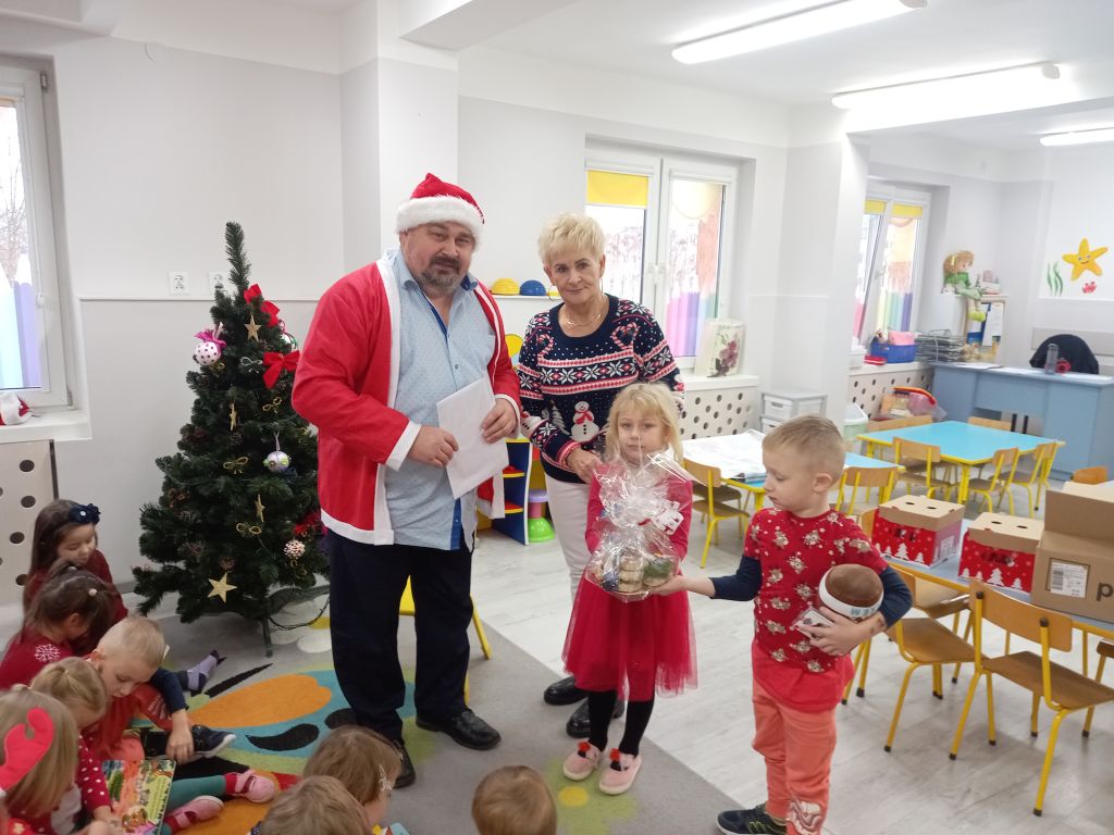 Zdjęcie przedstawia panią dyrektor przedszkola w Skępem Świętego Mikołaja wręczającą wraz dziećmi podziękowanie pomocnikowi w skępskim przedszkolu