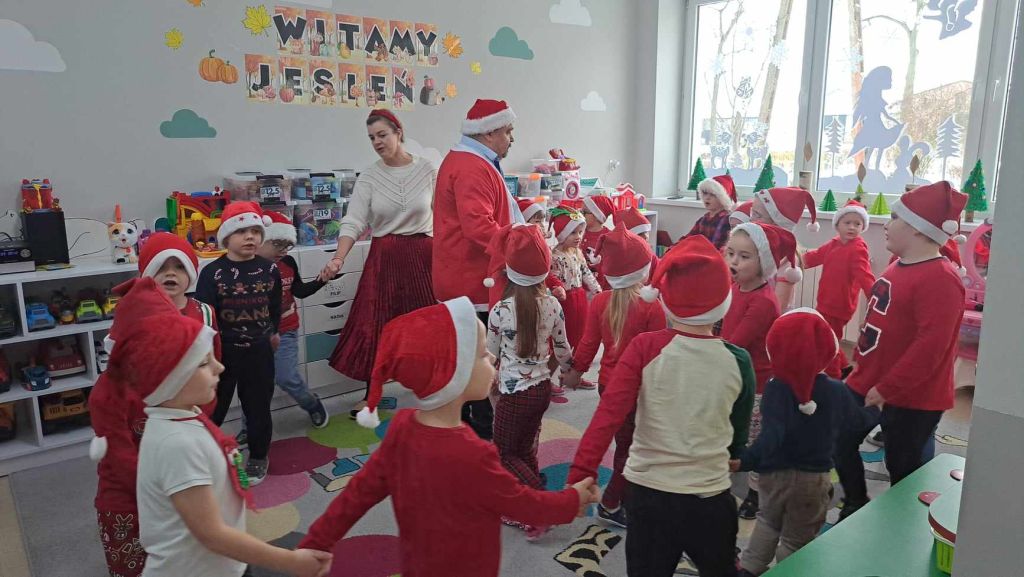 Zdjęcie przedstawia dzieci tańczące w kółeczku wraz z Mikołajem i wychowawczynią z przedszkola